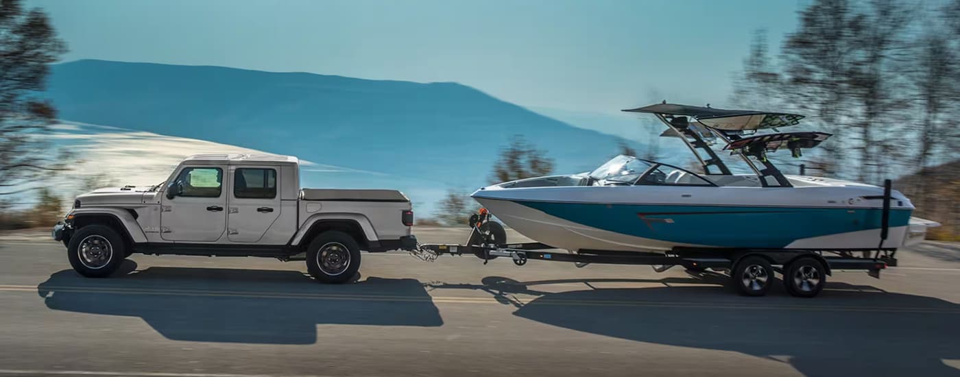 A silver 2023 Jeep Gladiator is shown from the side towing a boat.