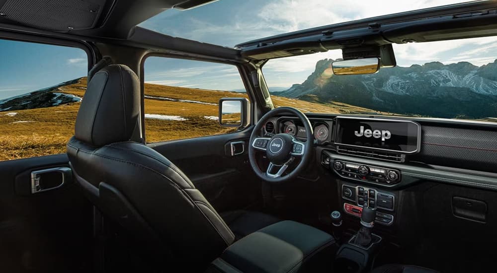 The interior of a 2024 Jeep Wrangler with moonroof and open windows, parked on a mountaintop.