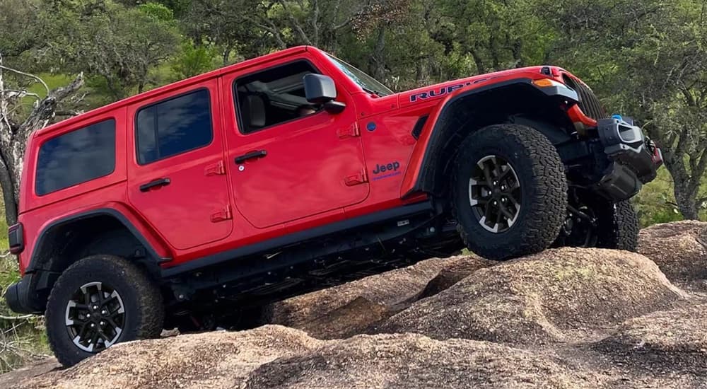 A red 2024 Jeep Wrangler Rubicon off-roading over large boulders.