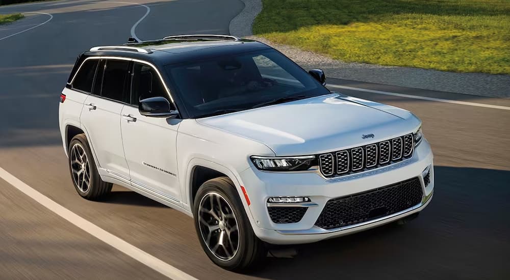 A white 2024 Jeep Grand Cherokee driving to a Jeep dealer on a winding road.