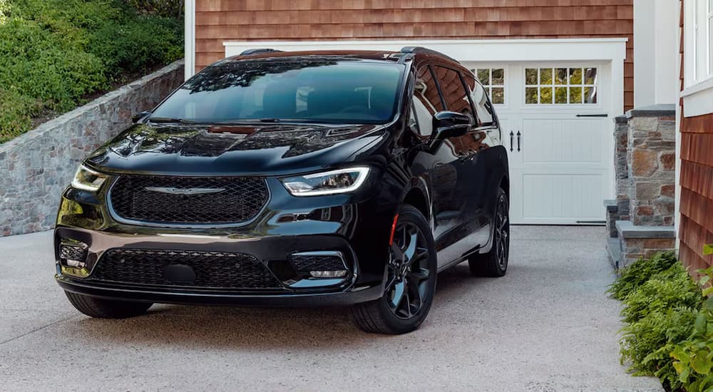 A black 2024 Chrysler Pacifica parked in front of a suburban home.