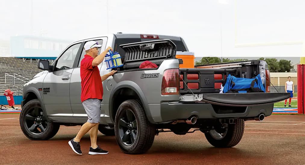 A coach loading sports gear into the bed of a grey 2019 Ram 1500 Classic Warlock.