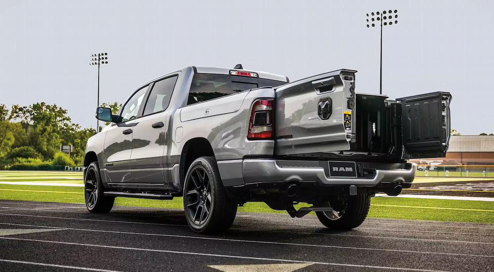 A silver 2024 Ram 1500 Laramie parked at a football field with the Multifunction Tailgate opened.