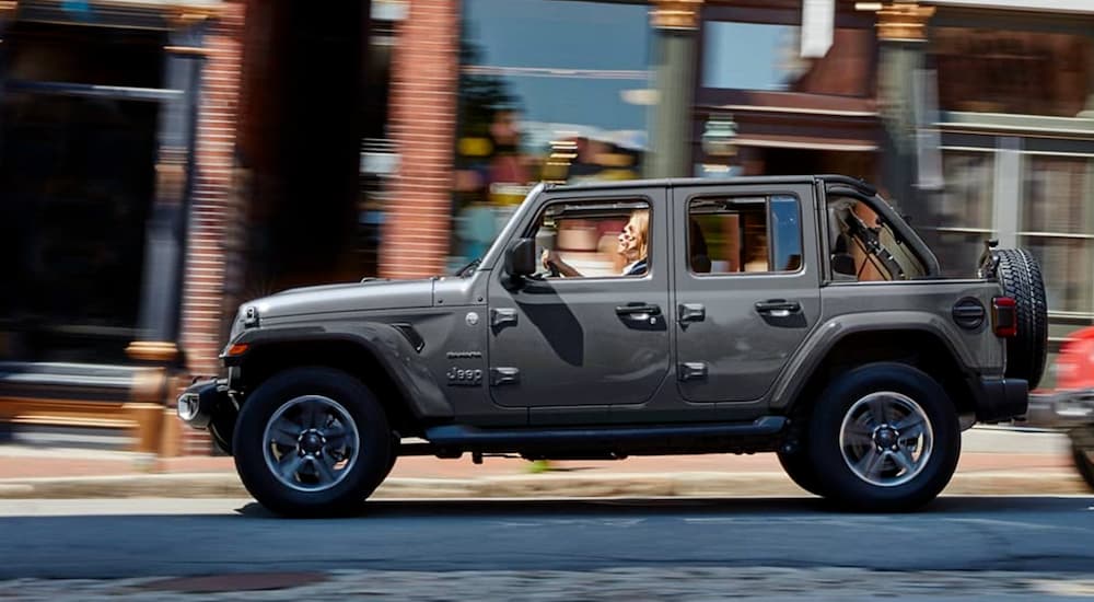 Side angle view of a black 2021 Jeep Wrangler Sahara Unlimited driving in a city.