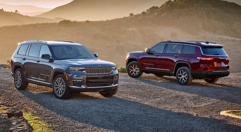 A grey and a red 2024 Jeep Grand Cherokee are parked during a sunset on gravel.