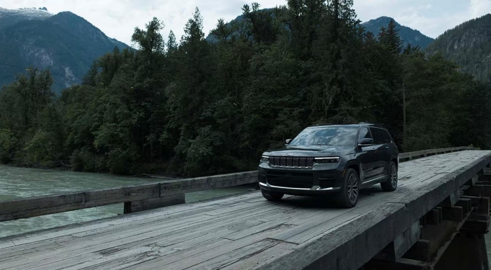 A grey 2024 Jeep Grand Cherokee for sale crossing a bridge.
