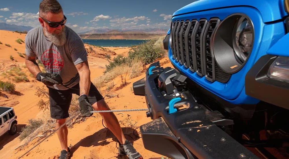 A person using a winch on a used blue 2024 Jeep Wrangler for sale.