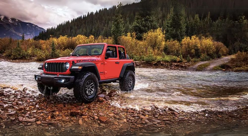 A red 2024 Jeep Wrangler parked near a river