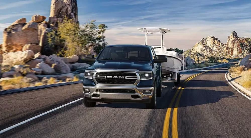 A blue 2023 Ram 1500 towing a boat on a highway.