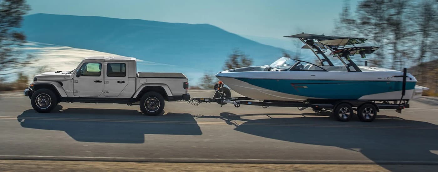 A silver 2023 Jeep Gladiator towing a boat after leaving a dealer that has used trucks for sale.