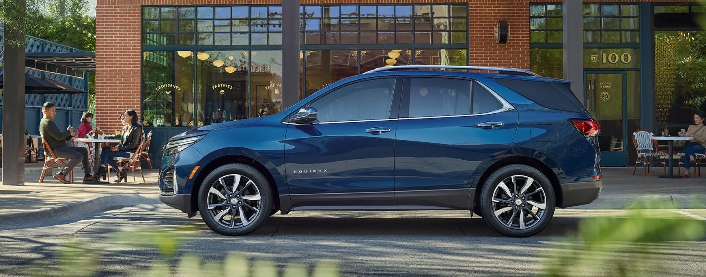 Side angle view of a blue 2022 Chevy Equinox parked by a used car dealership near Cambridge.
