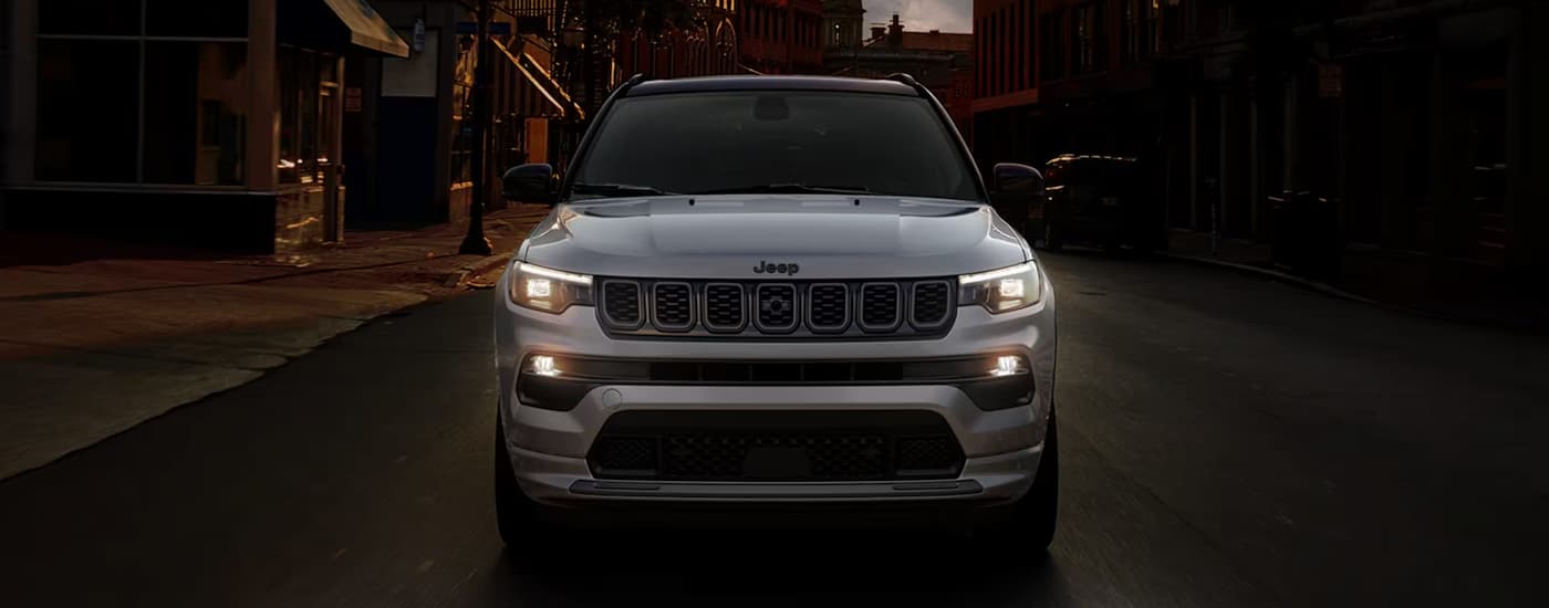A grey 2024 Jeep Compass is driving on a city street at night.