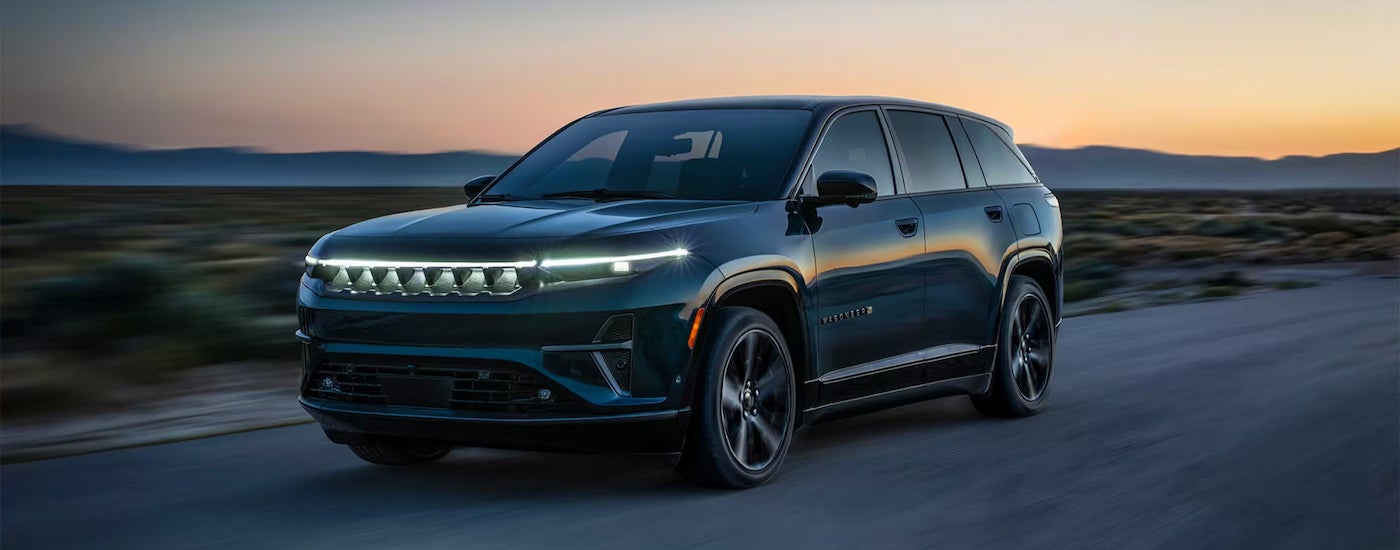 A dark blue 2024 Jeep Wagoneer S driving to a Jeep dealer near Newark at dusk.