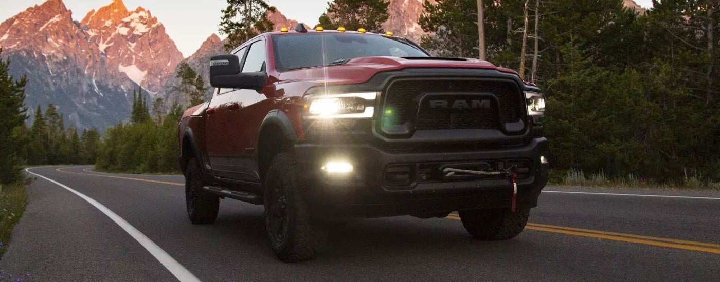 A red 2023 Ram 2500 is driving on a tree-lined road after visiting a Ram dealer.