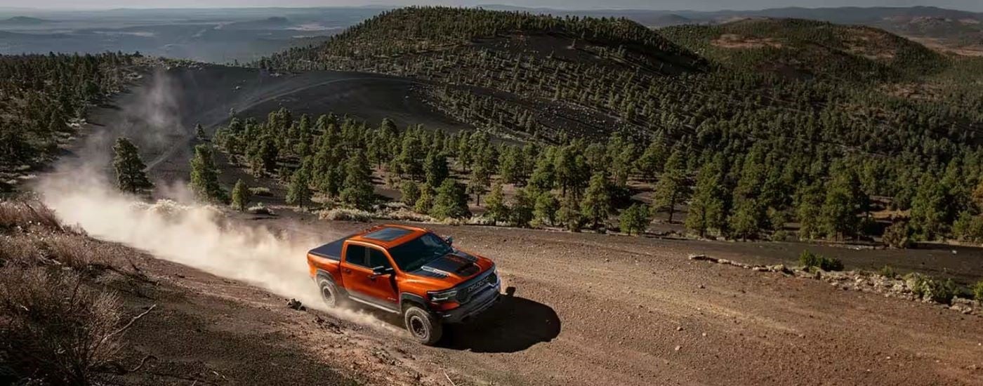 An orange 2024 Ram 1500 TRX Final Edition driving on a dusty mountain trail.