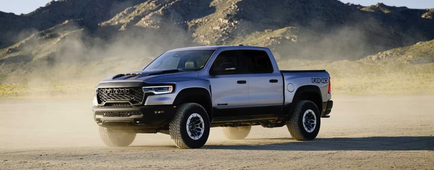 A silver 2025 Ram 1500 RHO is parked on a dusty dirt road.