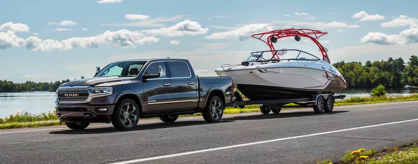 A black 2024 Ram 1500 is towing a boat next to a lake.