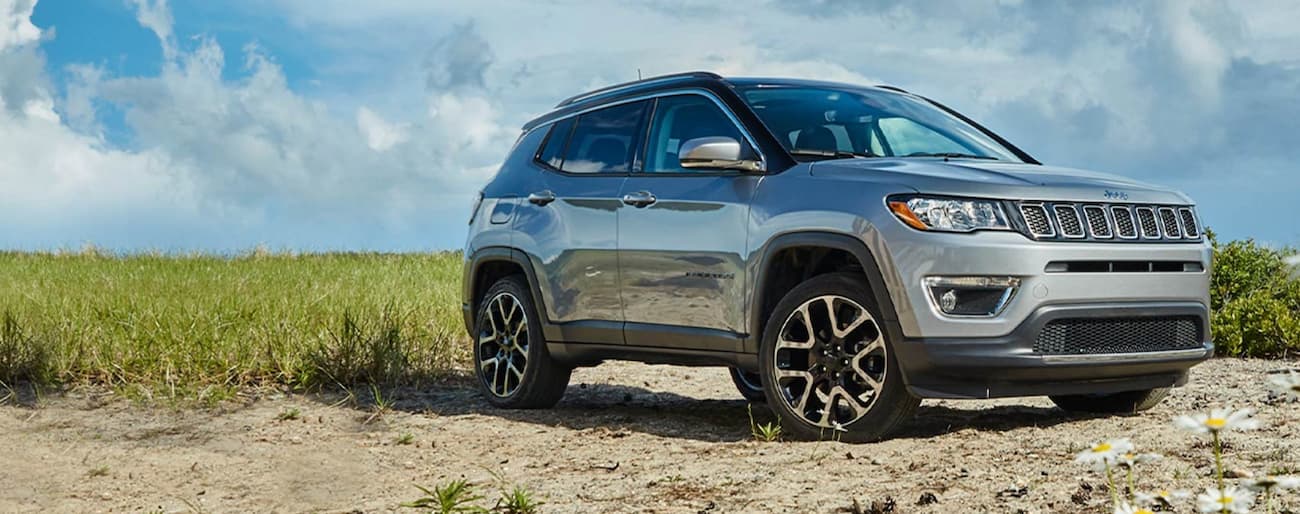 A grey 2020 Jeep Compass parked in a field after visiting a used car dealership.