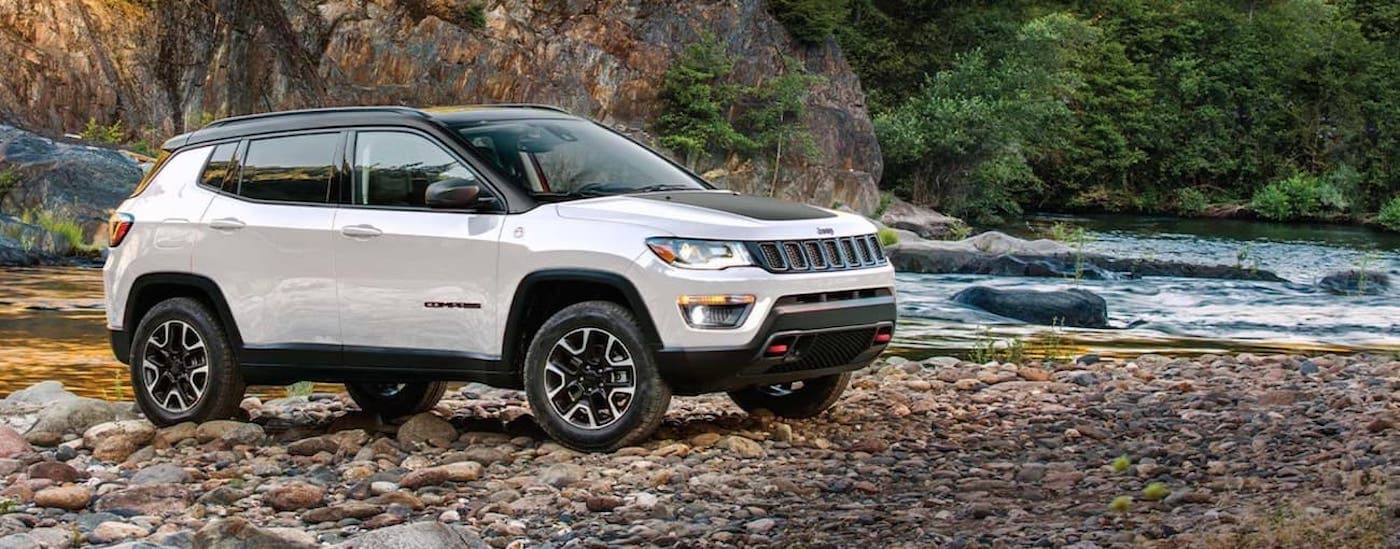A white and black 2020 Jeep Compass Trailhawk parked off-road by a river.