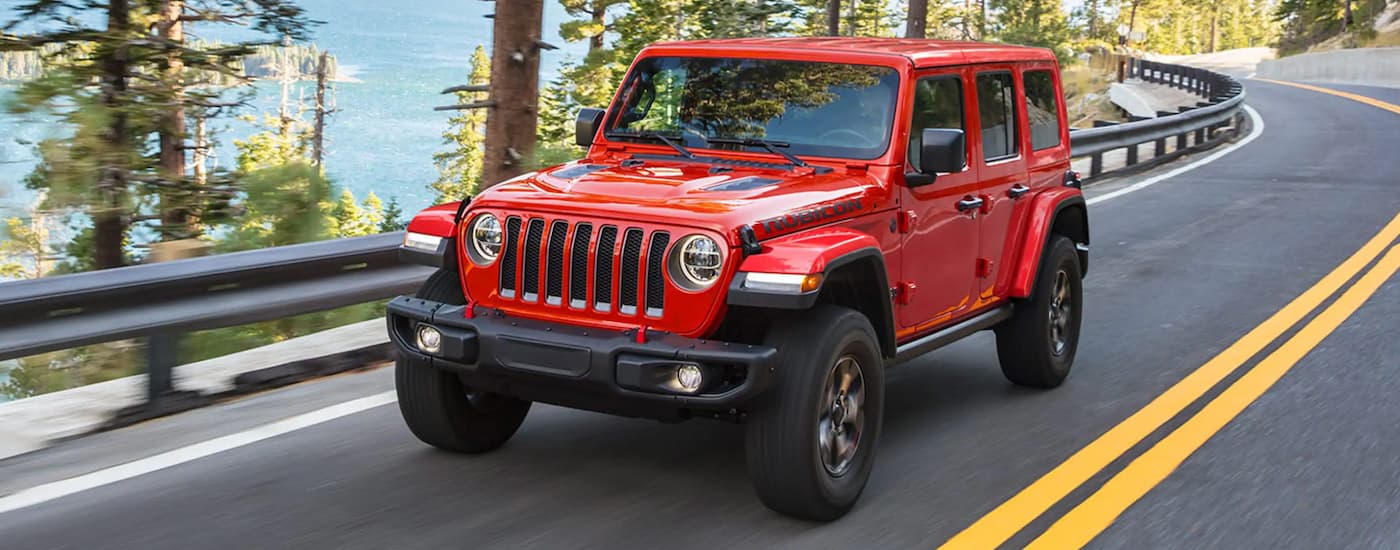 A red 2021 Jeep Wrangler Rubicon Unlimited driving from a used Jeep dealership.