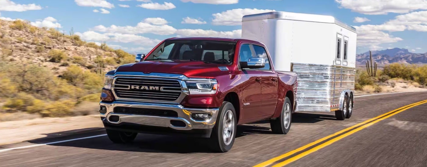 A red 2024 Ram 1500 Laramie towing a trailer on an open road.
